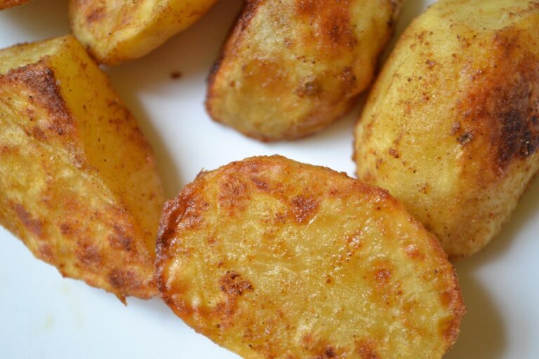 Patate al forno croccanti marinati, serviti su un piatto bianco con rosmarino fresco.